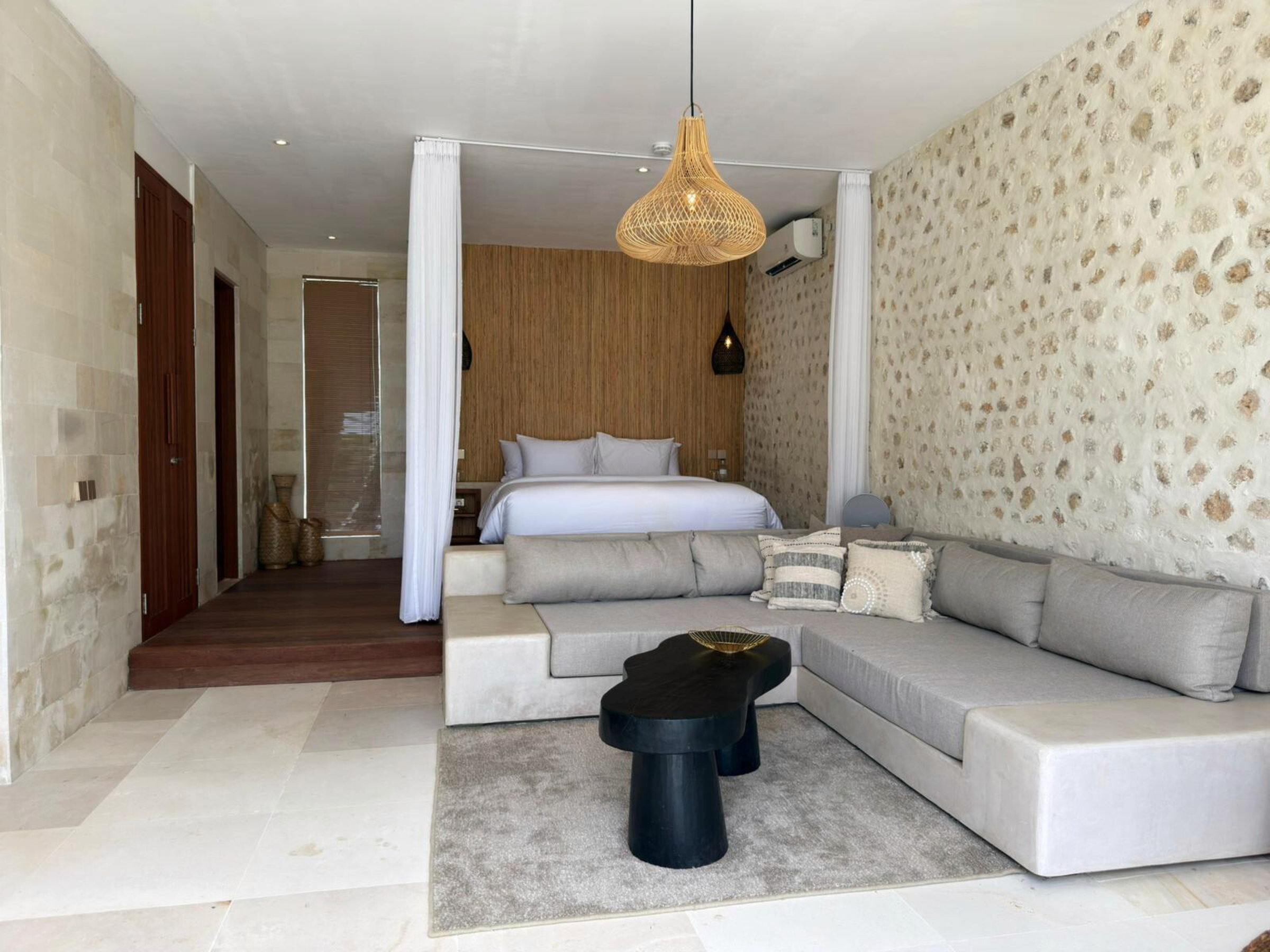 Interieur van het paviljoen met bed en witte gordijnen, grote sofa, stenen muren en rotan lampen