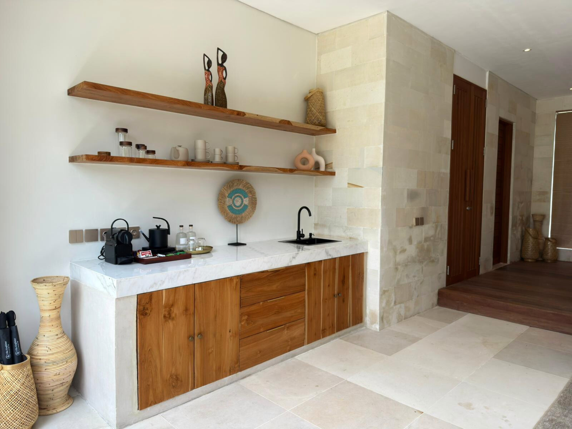 Kleine kitchenette met marmeren blad, houten kastjes, open planken en een koffiezetapparaat