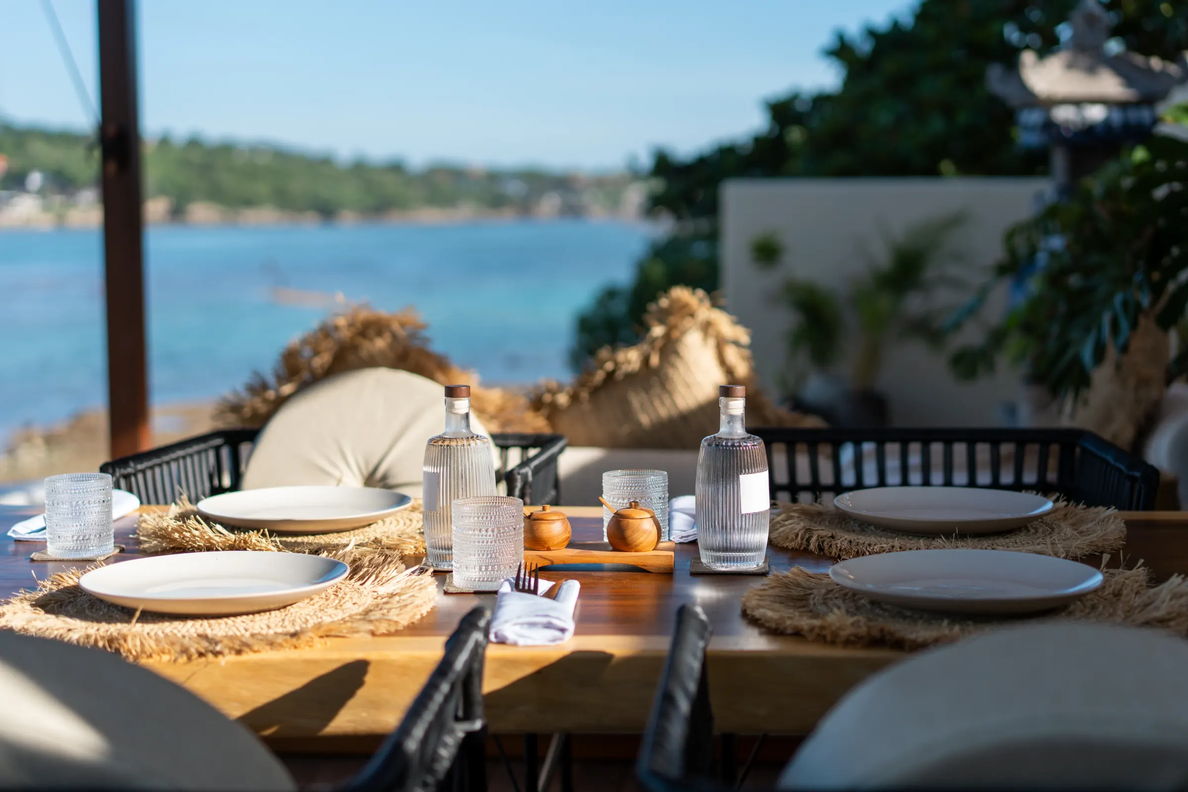 Table set for dinner on a terrace above the sea on Nusa Lembongan, with rattan placemats, ceramic plates and a view over the bay