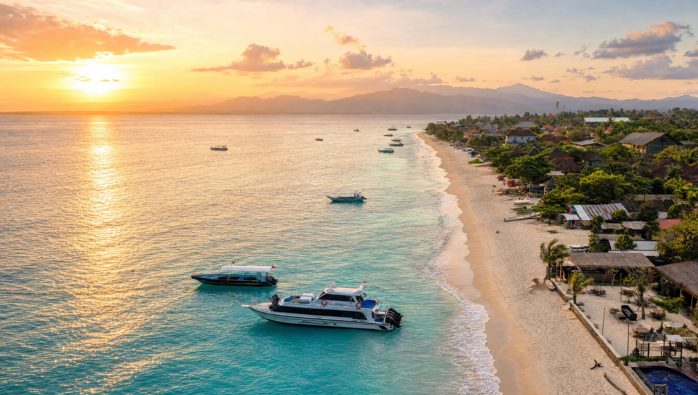 Sunset over the beach and calm water of Nusa Lembongan, with boats and mountains beyond